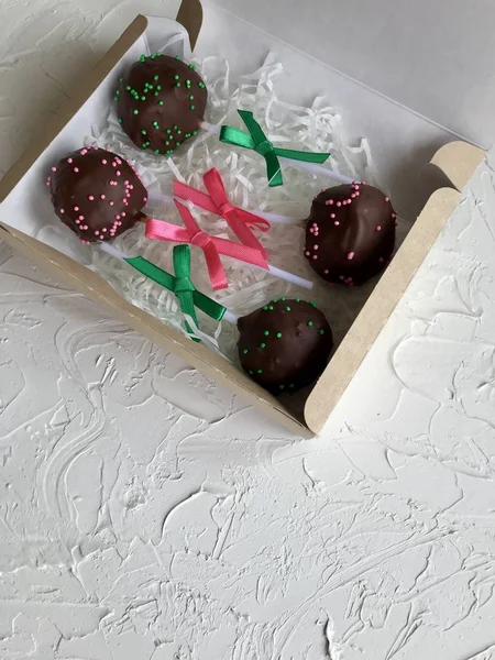 Cake pops decorated with a bow of braid, packed in a gift box.  On the surface covered with decorative plaster white.