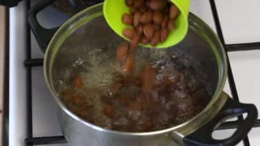 Bir adam kaynar su bir tencereye badem döker ve karıştırır. Çikolata kaplı tatlılar dolgu hazırlamak için.