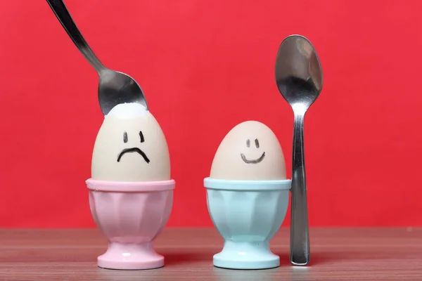 Ένα βραστό αυγό με κομμένο κέλυφος στέκεται σε ένα ποσέ. Στο αυγό που βάφτηκε χαμογελαστός. Ένα κουτάλι κόλλησε για φαγητό. Με φόντο το χρώμα των Κοραλλιών. — Φωτογραφία Αρχείου