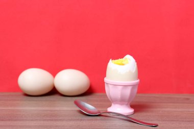 Boiled egg in poached pink. Next spoon for food. Against the background of coral color. clipart