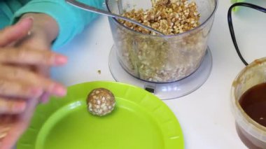 Bir kadın bir popcake dolgu için topları rulo ve bir tabak üzerine koyar. Diğer malzemelerle karıştırılmış ezilmiş fıstıktan.