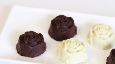 Beyaz bir tabak üzerinde siyah ve beyaz çikolata ile sırlı hazır şekerler vardır. Badem dolgulu.
