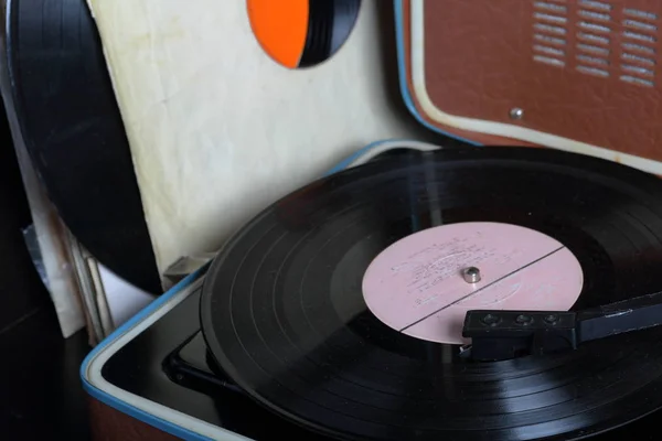 Un viejo gramófono con un disco de vinilo montado en él. Junto a sobres de papel de mala calidad hay otros registros . —  Fotos de Stock