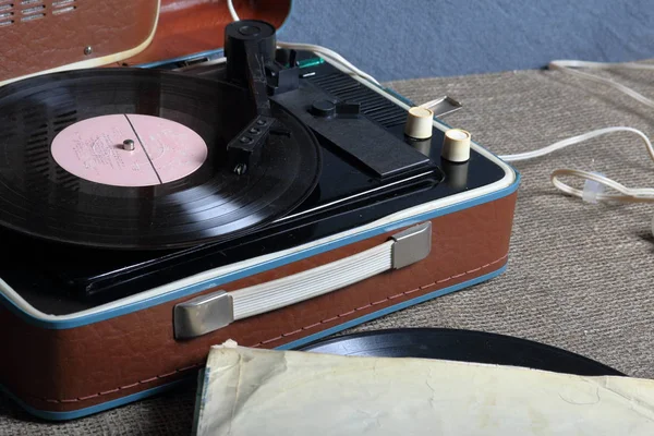 Un viejo gramófono con un disco de vinilo montado en él. Junto a sobres de papel de mala calidad hay otros registros . —  Fotos de Stock