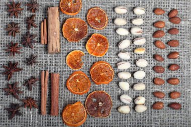 Kurutulmuş portakal dilimleri, tarçın ve dekorasyon için anason. Ayrıca antep fıstığı ve badem kaba keten kumaş üzerinde sırahalinde serilir.