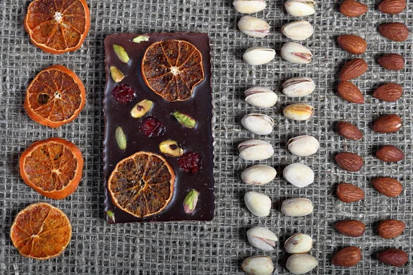 Dried orange slices, pistachios and almonds are lined up in rough linen fabric. Dark chocolate decorated with dried fruit.