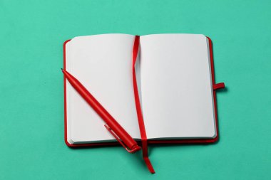 Kırmızı kapaktaki notlar için not defteri. Kırmızı bir yer imi ve kalemle. Nane arka planında açılan yalanlar. Okul malzemeleri.