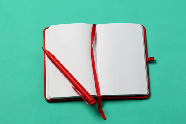 Notebook for notes in the red cover. With a red bookmark and pen. Lies opened on a mint background. School supplies.