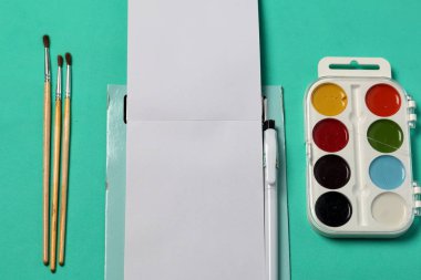 Çizim ve çizim için aksesuarlar. Nane rengi yüzeyinde çürümüş. Açık not defterinin ortasında. Okul malzemeleri.