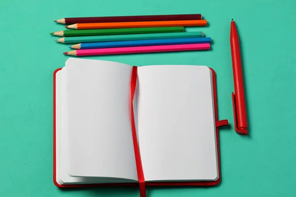 Caderno de notas na capa vermelha. Com um marcador vermelho e uma caneta. Mentiras abertas em um fundo de hortelã. Em seguida, é um conjunto de lápis de cor. Material escolar . — Fotografia de Stock
