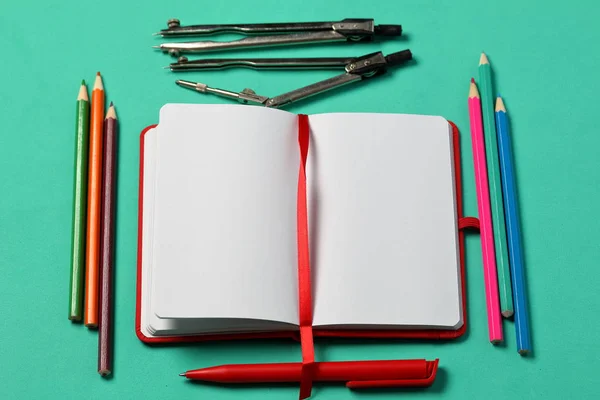 Caderno de notas na capa vermelha. Com um marcador vermelho e uma caneta. Mentiras abertas em um fundo de hortelã. Ao lado de um conjunto de lápis coloridos e acessórios para desenho. Material escolar . — Fotografia de Stock