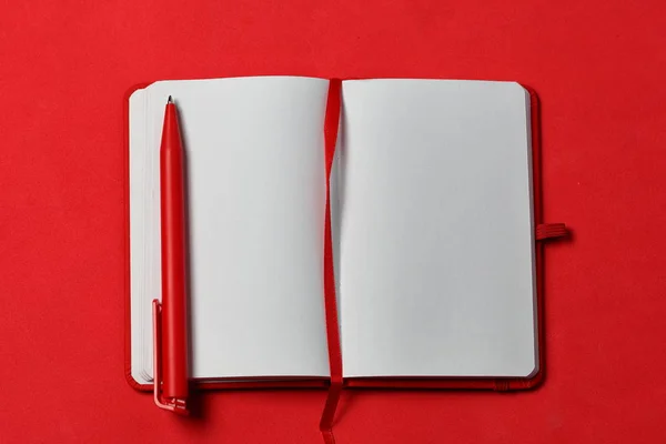 Carnet de notes sur la couverture rouge. Avec un signet rouge et un stylo. Les mensonges s'ouvrent sur un fond de corail. Fournitures scolaires . — Photo