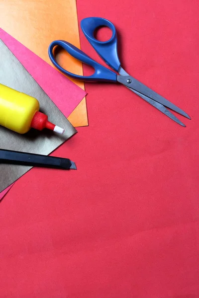Accessoires voor toepassing. Schaar, mes, kleur papier, potlood en liniaal. Tegen de achtergrond van koraal kleur. — Stockfoto