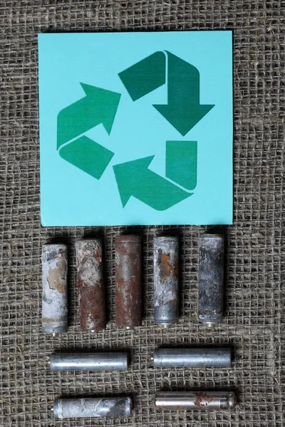 Baterias usadas estão em um fundo de linho áspero. Coberto de corrosão. Nas proximidades é o sinal de reciclagem do loop M=bius. Reciclagem e protecção do ambiente . — Fotografia de Stock