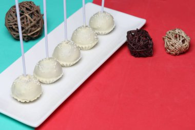 Kek beyaz çikolata sır açılır. Bir stand üzerinde dikey olarak durun. Beyaz dekoratif serpmelerle dekore edilmiştir. Rattan topları yakınında.