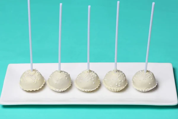 Cake pops in white chocolate glaze. Stand vertically on a stand. Decorated with white decorative sprinkles. On a mint background. — Stock Photo, Image