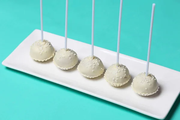 Cake pops in white chocolate glaze. Stand vertically on a stand. Decorated with white decorative sprinkles. On a mint background. — Stock Photo, Image