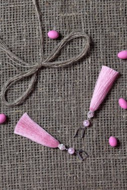 Küpeler, püsküller kaba keten kumaş üzerinde yatıyor. Yakındaki keten ve çakıl bir yay.