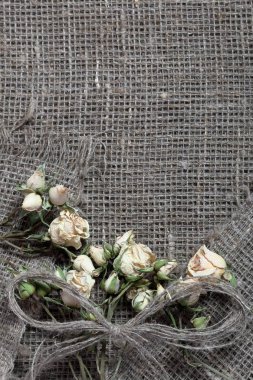 Kaba keten kumaş. Üzerinde kurutulmuş bej gül ve keten iplikleri bir yay vardır.