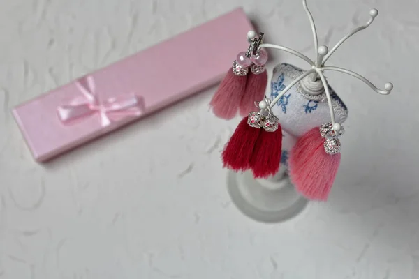 Earrings, tassels hang on a special stand. Next packing box with a bow. View from above.
