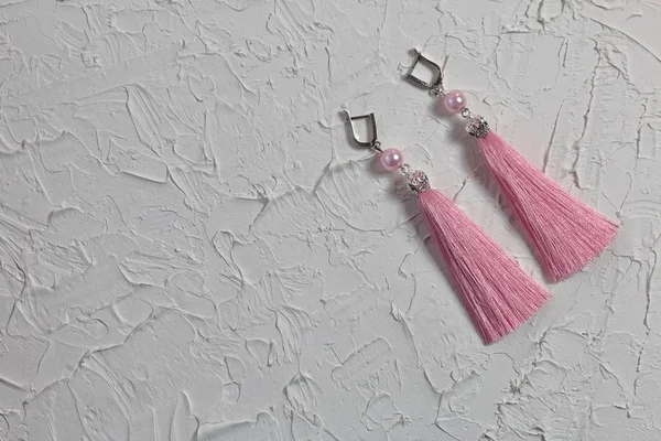Earrings tassels. They lie on the surface covered with white decorative plaster. — Stock Photo, Image