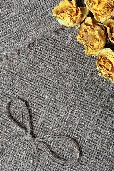 Tessuto di lino grezzo. Su di esso sono essiccate rose gialle e un fiocco di fili di lino . — Foto Stock