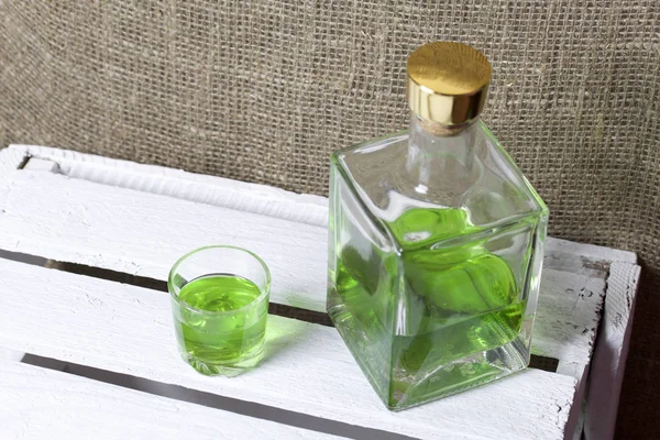 Silna Nalewka na Tarhuna w przezroczystej prostokątnej butelce. Pić jasny zielony wlewa się w szklankę. — Zdjęcie stockowe