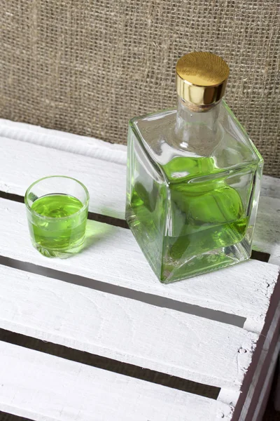 Silna Nalewka na Tarhuna w przezroczystej prostokątnej butelce. Pić jasny zielony wlewa się w szklankę. — Zdjęcie stockowe