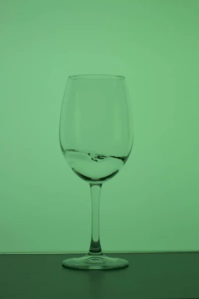 Verre à vin sur une longue tige. Un peu de boisson y est versé, une éclaboussure est visible. Dans le dos vert . — Photo