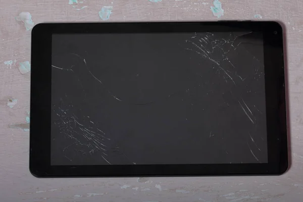 Tablet with a broken screen lies on the surface with a shabby paint.