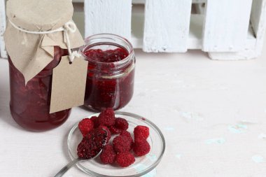 Reçel kavanozları, kağıt ile kaplıdır ve ikiyle bağlanmış. Dize asmak Craft etiketleri. Bir kavanoz açık. Taze ahududu bir plaka yanında.