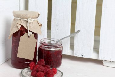 Reçel kavanozları, kağıt ile kaplıdır ve ikiyle bağlanmış. Dize asmak Craft etiketleri. Bir kavanoz açık. Taze ahududu bir plaka yanında.