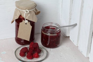 Reçel kavanozları, kağıt ile kaplıdır ve ikiyle bağlanmış. Dize asmak Craft etiketleri. Bir kavanoz açık. Taze ahududu bir plaka yanında.