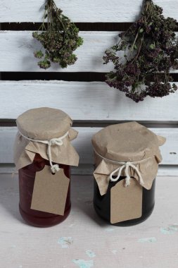 Reçel kavanozları, kağıt ile kaplıdır ve ikiyle bağlanmış. Dize asmak Craft etiketleri. Yeşil ve baharatların Tufts yakınında. Ahşap tahtaları arka planda.