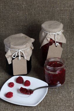 Reçel kavanozları, kağıt ile kaplıdır ve ikiyle bağlanmış. Dize asmak Craft etiketleri. Bir kavanoz açık. Bir plaka üzerinde taze ahududu yakın.