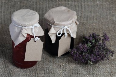 Reçel kavanozları, kağıt ile kaplıdır ve ikiyle bağlanmış. Dize asmak Craft etiketleri. Yeşil ve baharatların Tufts yakınında. Keten kaba kumaş zemin karşı.