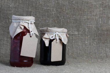 Reçel kavanozları, kağıt ile kaplıdır ve ikiyle bağlanmış. Dize asmak Craft etiketleri. Keten kaba kumaş zemin karşı.