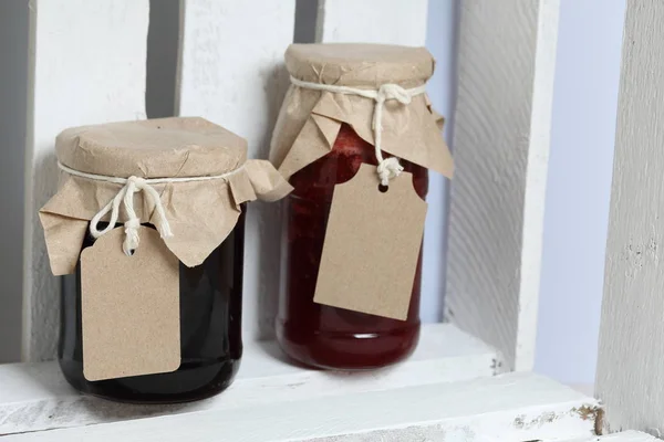 Pots de confiture, recouverts de papier et attachés avec de la ficelle. Sur la ficelle accrocher des étiquettes artisanales. Stand dans une boîte en bois . — Photo