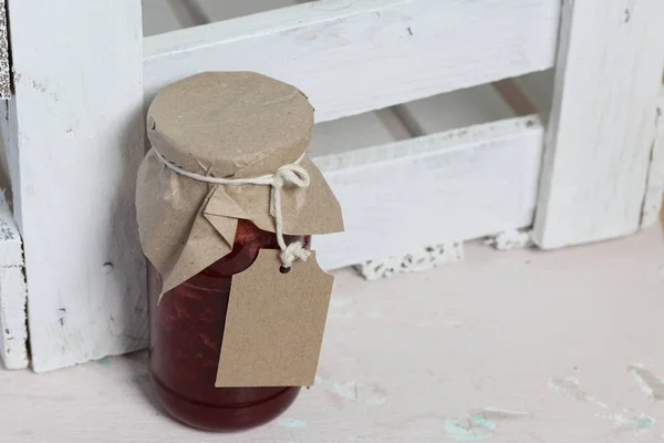 Pots de confiture, recouverts de papier et attachés avec de la ficelle. Sur la ficelle accrocher des étiquettes artisanales. Sur le fond des planches en bois . — Photo