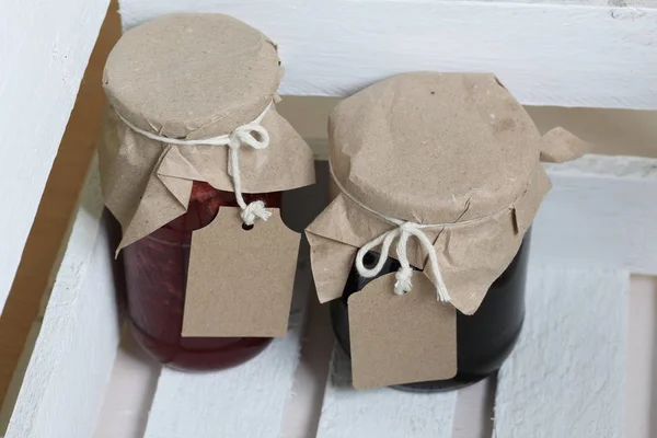 Vasetti di marmellata, ricoperti di carta e legati con spago. Sulla corda appendere etichette artigianali. Stand in una scatola di legno . — Foto Stock