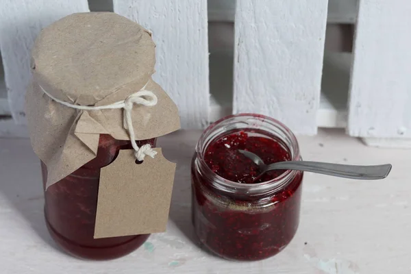 Pots de confiture, recouverts de papier et attachés avec de la ficelle. Sur la ficelle accrocher des étiquettes artisanales. Un pot est ouvert . — Photo