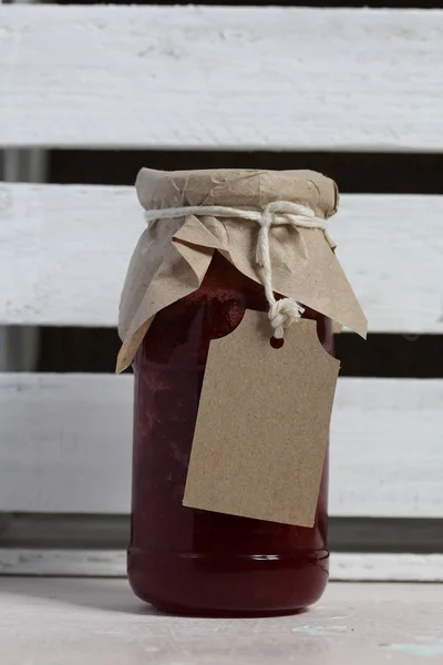 Pots de confiture, recouverts de papier et attachés avec de la ficelle. Sur la ficelle accrocher des étiquettes artisanales. Sur le fond des planches en bois . — Photo