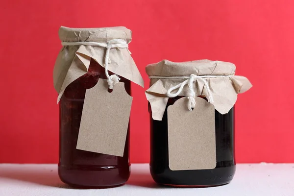 Pots de confiture, recouverts de papier et attachés avec de la ficelle. Sur la ficelle accrocher des étiquettes artisanales. Sur fond de couleur corail . — Photo