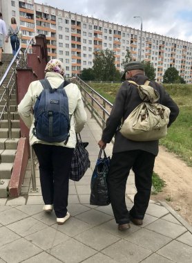 Minsk, Minsk, Belarus 7 Temmuz 2019, onların yaz yazlık yaşlı bir çift döner. Bunların arkasında, torbada ağır sırt çantaları var..
