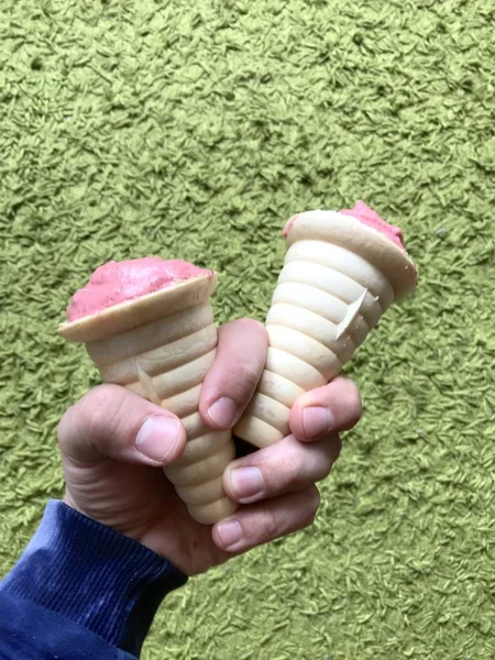 Um homem segura na mão duas porções de gelado. Sorvete nos chifres, tem uma cor de coral. Em um fundo verde . — Fotografia de Stock