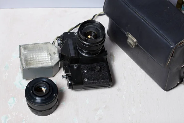 Old film camera, removable lens and wired flash. They lie on the surface of the table.