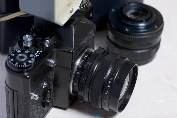 Old film camera, removable lens and wired flash. They lie on the surface of the table.