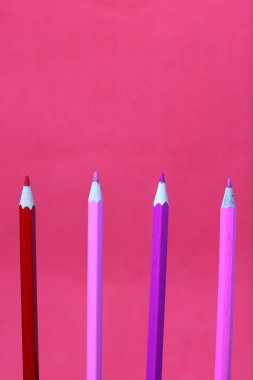 Mercan ve pembe renkli kalemler. Dikey olarak bulunurlar. Mercan renginin arka planına karşı.