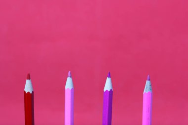 Mercan ve pembe renkli kalemler. Dikey olarak bulunurlar. Mercan renginin arka planına karşı.