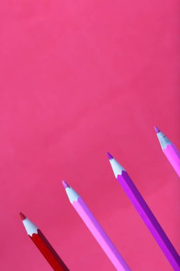 Mercan ve pembe renkli kalemler. Dikey olarak bulunurlar. Mercan renginin arka planına karşı.